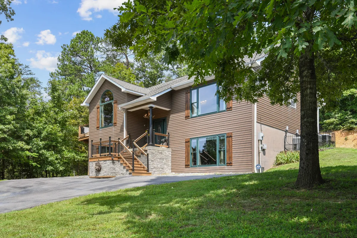The image features a two-story cabin with a mix of stone and wood accents, expansive windows, and a landscaped front yard. The inviting outdoor space is ideal for family gatherings, barbecues, or simply relaxing on the porch.