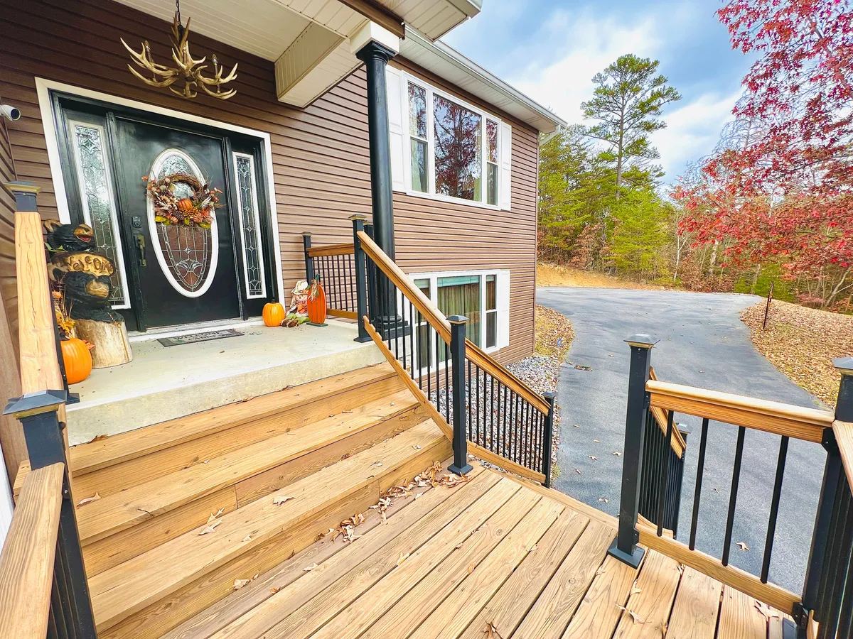 A welcoming front door adorned with a decorative wreath and pumpkins, wooden steps leading up, and an antler chandelier glimpsed through the window. The scene radiates warmth and seasonal festivity, inviting visitors into the home.