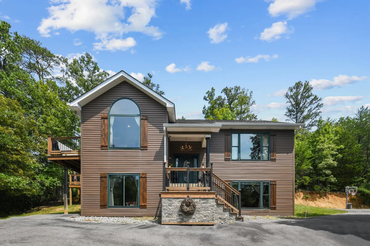 This exterior image showcases a modern cabin with large windows, wooden shutters, and a welcoming front porch. The architecture blends contemporary design with rustic touches, and the spacious porch invites guests to gather and enjoy the outdoors.