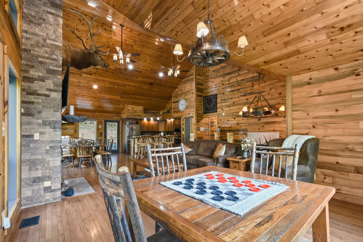 The focus here is on a broad wooden dining table set with a checkers game, surrounded by comfortable seating and backed by a dramatic stone feature wall. The space radiates warmth and invites both playful family competition and cozy mealtime conversation.