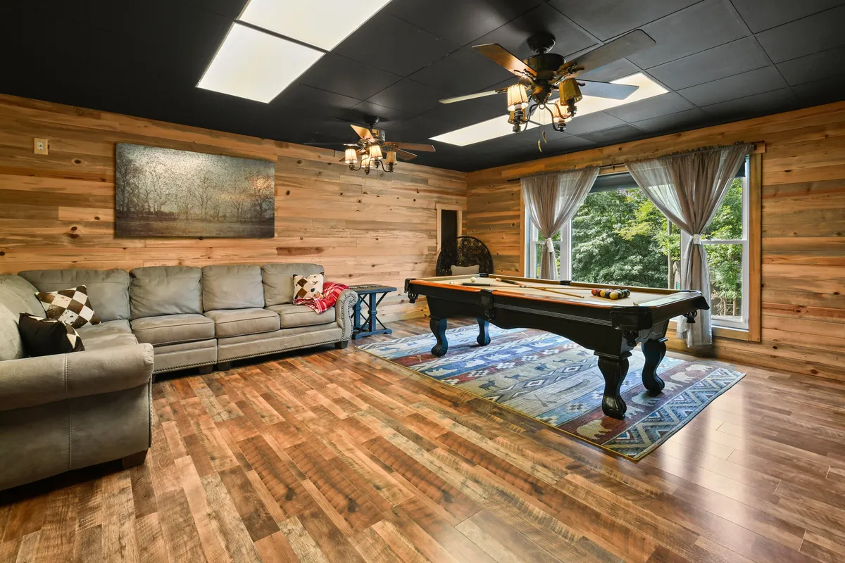An inviting game room with a pool table, large window letting in natural light, a comfortable sofa, and wall art, creating a lively and casual space for friendly competition and relaxation.
