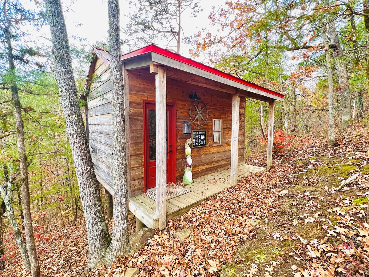 This image depicts a cozy wooden cabin nestled amidst lush natural surroundings. The red door and tasteful decorative elements add to its inviting charm, while the abundant greenery highlights the cabin's proximity to nature and outdoor adventure.