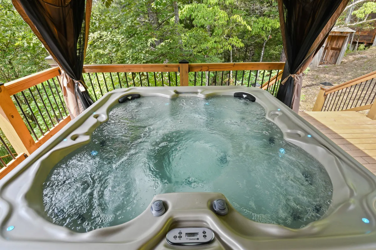 A tranquil wooden deck features a bubbling hot tub surrounded by vibrant greenery, inviting guests to relax and enjoy the natural setting. The open-air environment hints at rejuvenating evenings under the stars or mornings with coffee in hand.