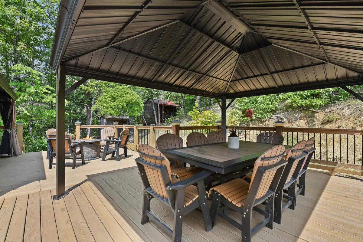A sizable outdoor dining table under a canopy, surrounded by greenery. The scene is set for a group meal in nature, with plenty of seating and a backdrop of trees that enhance the woodland retreat feeling.