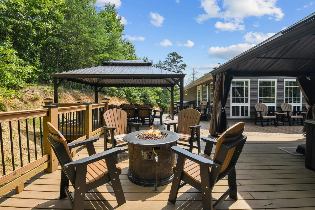 A welcoming fire pit encircled by Adirondack chairs sits beneath a gazebo, with tall trees providing a serene backdrop. The scene is set for communal gatherings, storytelling, and stargazing after busy days out.